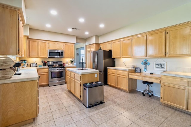 kitchen with sink, built in desk, light tile patterned floors, appliances with stainless steel finishes, and a kitchen island