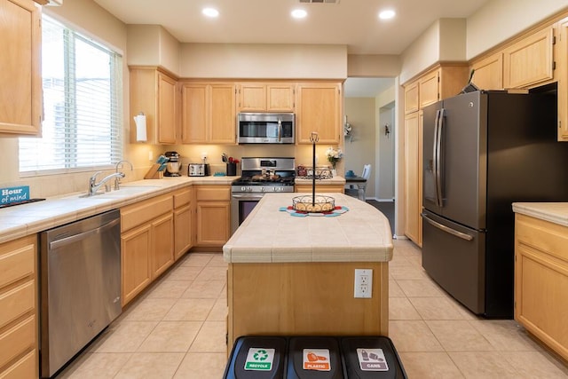 kitchen featuring tile countertops, a center island, light tile patterned floors, light brown cabinetry, and appliances with stainless steel finishes