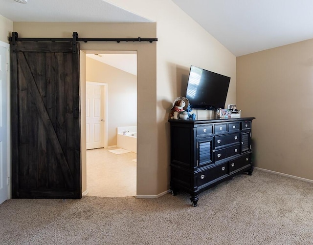 carpeted bedroom with a barn door, lofted ceiling, and ensuite bath