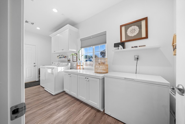 clothes washing area with washer and dryer, cabinets, and light wood-type flooring