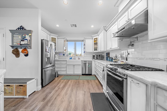 kitchen featuring appliances with stainless steel finishes, light wood-type flooring, light stone counters, extractor fan, and white cabinetry