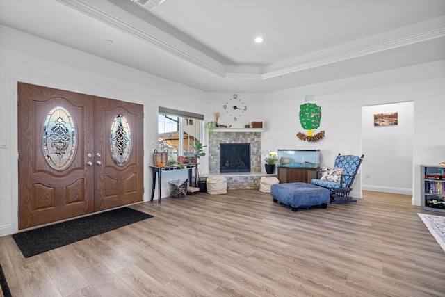 foyer entrance with a raised ceiling, a stone fireplace, and light hardwood / wood-style floors