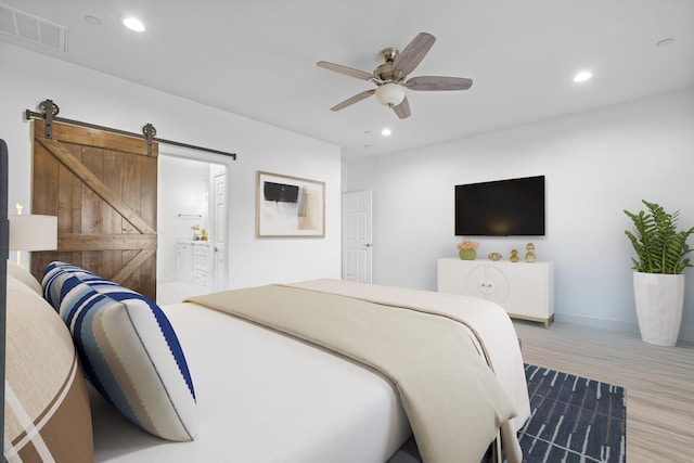 bedroom with a barn door, light hardwood / wood-style flooring, ensuite bath, and ceiling fan