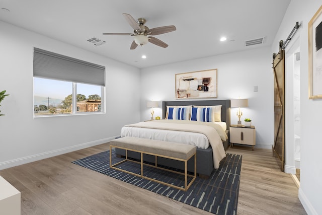 bedroom with light wood-type flooring, a barn door, and ceiling fan