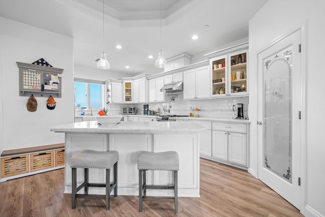 kitchen featuring white cabinets, hanging light fixtures, decorative backsplash, a kitchen island, and range