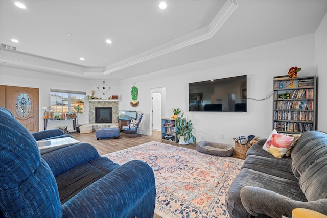 living room with a stone fireplace, wood-type flooring, crown molding, and a tray ceiling