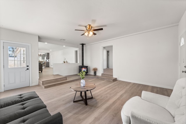 living room featuring ceiling fan, light hardwood / wood-style floors, and a wood stove