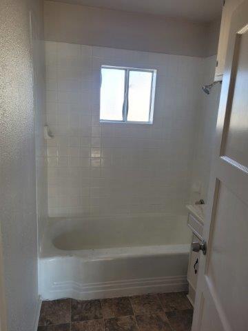 bathroom featuring stone finish floor and shower / bathing tub combination