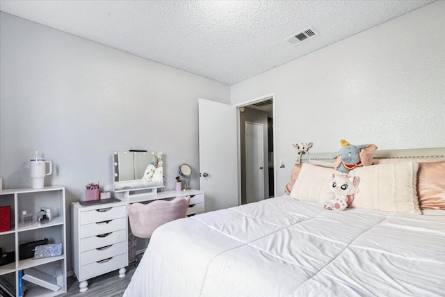 bedroom with wood finished floors, visible vents, and a textured ceiling