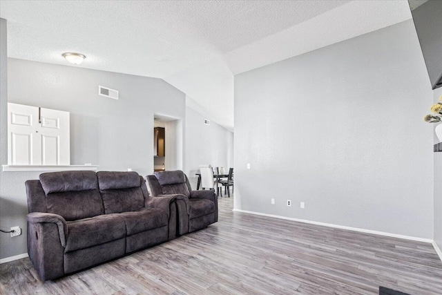 living room with visible vents, lofted ceiling, light wood-style floors, and baseboards