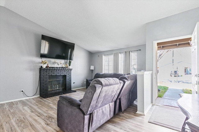 living area featuring light wood-style flooring, a fireplace, a textured ceiling, and baseboards