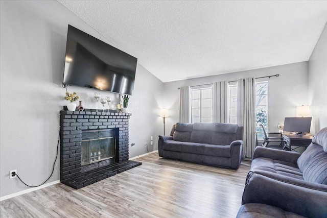 living room with baseboards, a textured ceiling, a brick fireplace, and wood finished floors