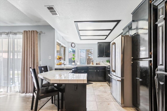 kitchen featuring visible vents, tile counters, a breakfast bar area, dark cabinetry, and black appliances