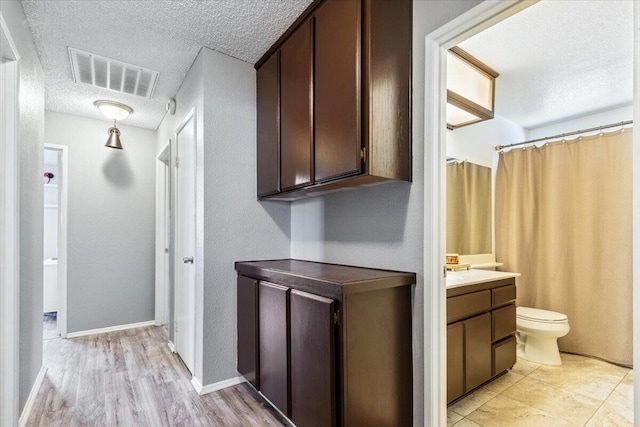 corridor with visible vents, light wood-style flooring, a textured ceiling, and baseboards