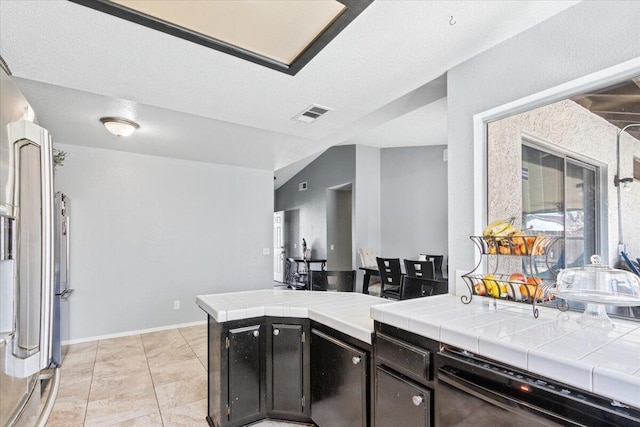 kitchen featuring visible vents, tile countertops, dishwasher, and lofted ceiling