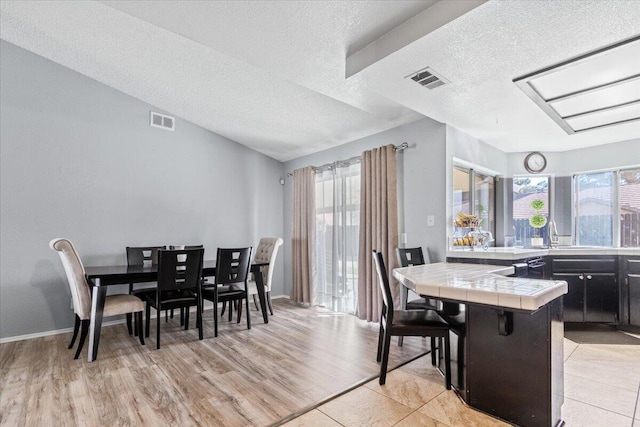 dining area with light wood finished floors, visible vents, and a textured ceiling