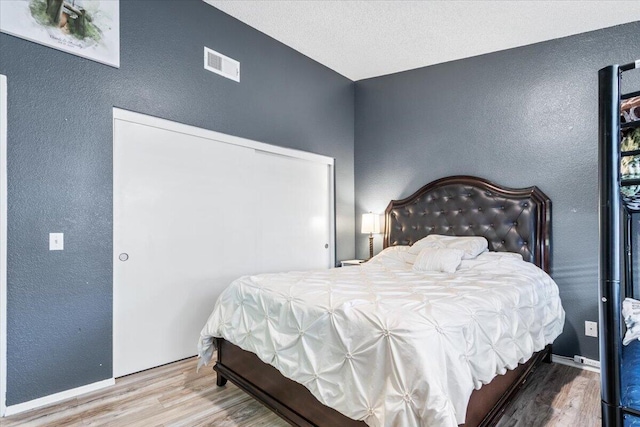 bedroom featuring visible vents, baseboards, wood finished floors, and a textured wall