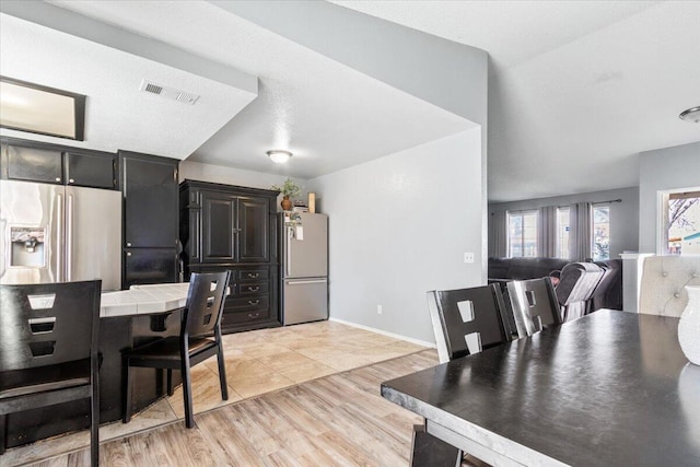 kitchen featuring tile countertops, visible vents, freestanding refrigerator, stainless steel refrigerator with ice dispenser, and light wood-type flooring