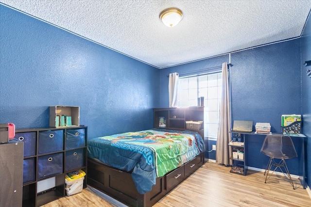 bedroom with a textured ceiling, wood finished floors, baseboards, and a textured wall