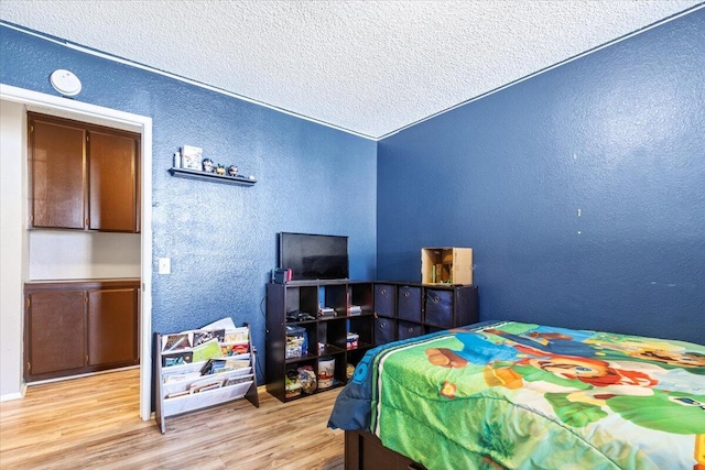 bedroom with a textured ceiling, wood finished floors, and a textured wall