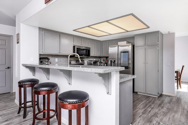 kitchen featuring stainless steel appliances, a kitchen breakfast bar, tasteful backsplash, kitchen peninsula, and gray cabinets