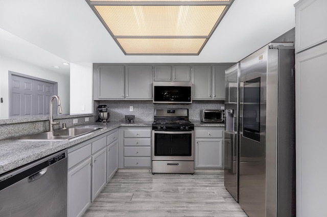 kitchen with gray cabinetry, sink, stainless steel appliances, and light hardwood / wood-style flooring