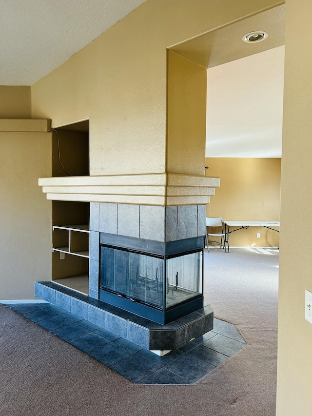 interior details featuring a tile fireplace, built in features, and carpet floors