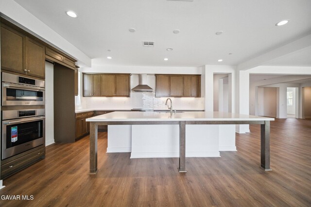 39635 Nicholas Ct, Palmdale, CA 93551 - kitchen with wall chimney exhaust hood, double oven, a center island with sink, light countertops, and tasteful backsplash
