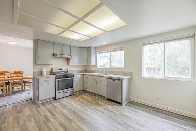43661 Bravo Ln, Lancaster, CA 93535 - kitchen featuring stainless steel appliances, gray cabinetry, under cabinet range hood, and light wood finished floors