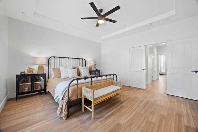 bedroom featuring baseboards, a raised ceiling, light wood-style floors, and a ceiling fan