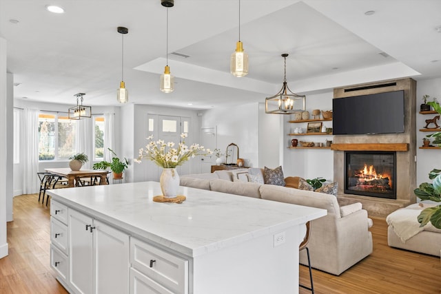 kitchen with light wood-style flooring, a raised ceiling, open floor plan, and white cabinets