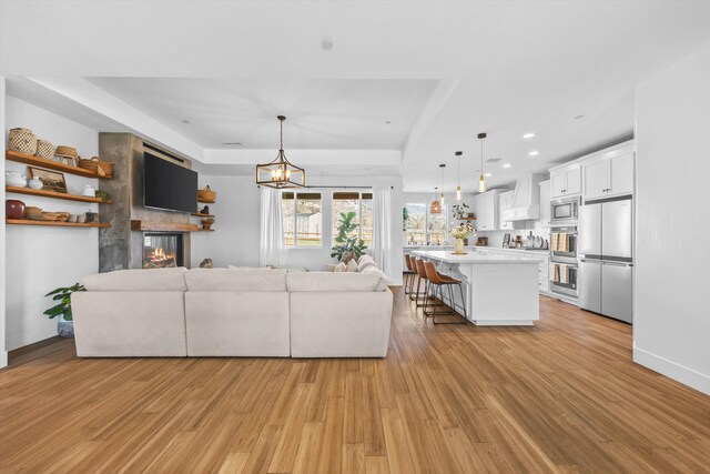 unfurnished living room featuring baseboards, a tray ceiling, recessed lighting, a glass covered fireplace, and light wood-type flooring