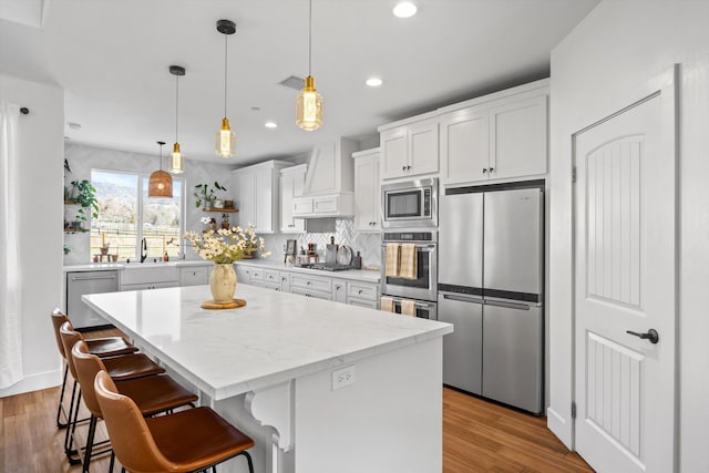 kitchen with custom range hood, wood finished floors, a center island, white cabinetry, and appliances with stainless steel finishes