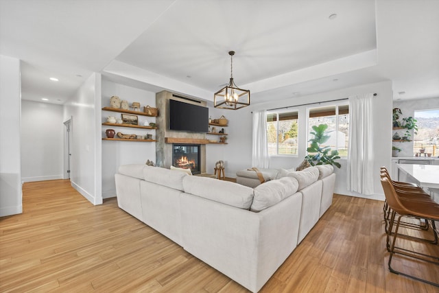 living room with a glass covered fireplace, a raised ceiling, baseboards, and light wood-type flooring