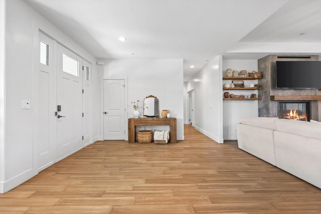 entrance foyer with a glass covered fireplace, recessed lighting, light wood-type flooring, and baseboards