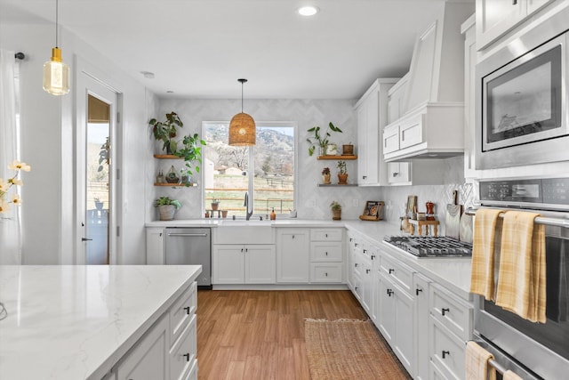 kitchen with light wood finished floors, open shelves, white cabinets, stainless steel appliances, and a sink