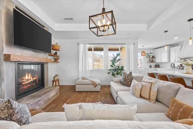 living room with wood finished floors, visible vents, baseboards, a high end fireplace, and a raised ceiling