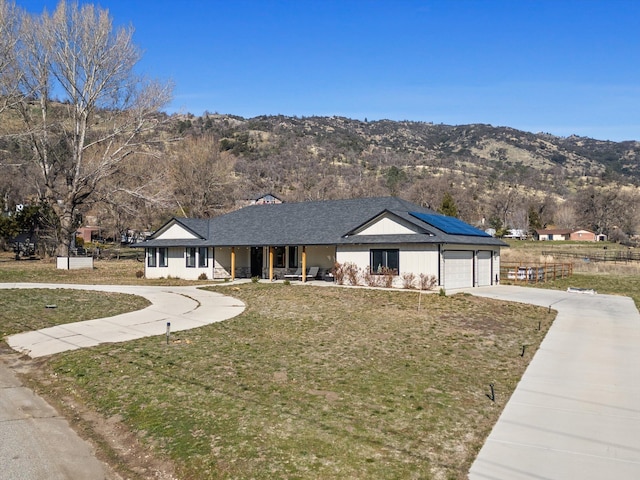 ranch-style house featuring a front lawn, a porch, roof mounted solar panels, driveway, and an attached garage