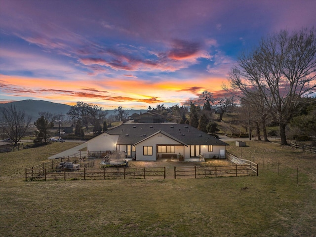 back of house at dusk featuring a yard, a patio area, a mountain view, and a fenced backyard