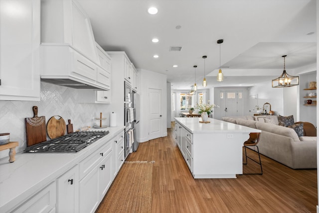 kitchen with tasteful backsplash, open floor plan, appliances with stainless steel finishes, white cabinets, and light wood finished floors