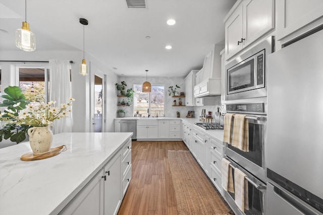 kitchen featuring light wood finished floors, open shelves, stainless steel appliances, custom range hood, and white cabinets