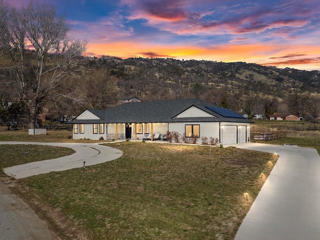 view of front of property with a front yard, an attached garage, concrete driveway, a mountain view, and roof mounted solar panels