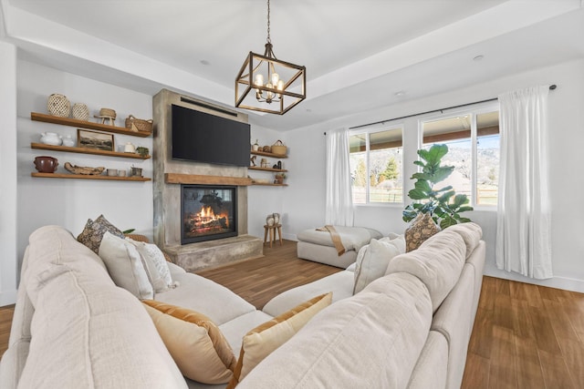 living area with a fireplace, a raised ceiling, baseboards, and wood finished floors