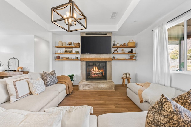 living area featuring wood finished floors, visible vents, a glass covered fireplace, a raised ceiling, and a chandelier