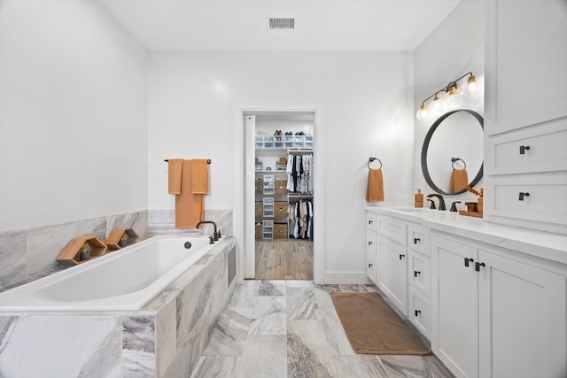 bathroom with visible vents, a walk in closet, a garden tub, marble finish floor, and vanity