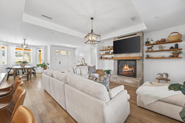 living area with visible vents, a raised ceiling, light wood-style floors, and a glass covered fireplace