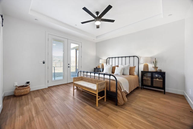 bedroom featuring a tray ceiling, access to outside, light wood-style floors, and baseboards