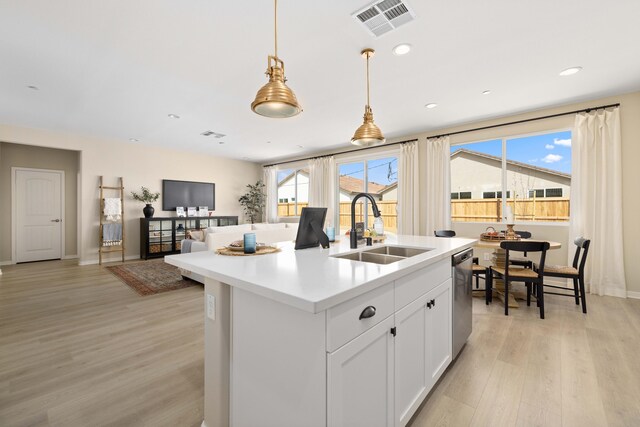 kitchen with an island with sink, a sink, light wood-type flooring, stainless steel dishwasher, and visible vents
