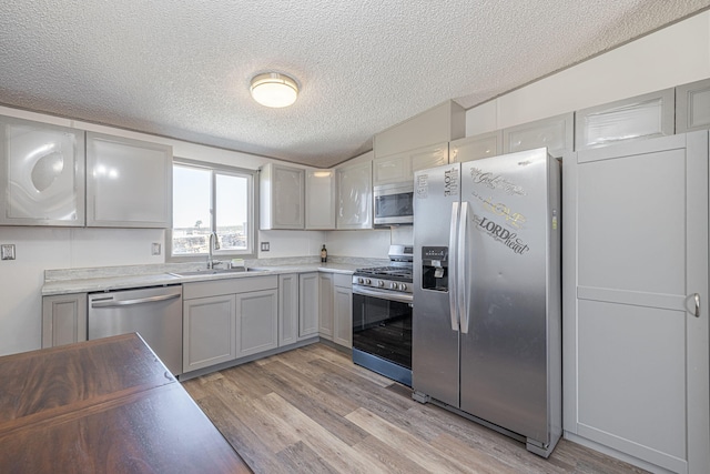 kitchen featuring gray cabinetry, sink, light wood-type flooring, a textured ceiling, and stainless steel appliances