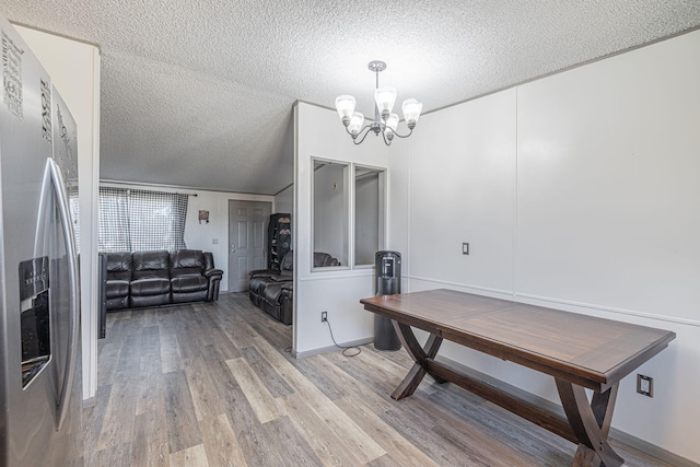 dining room with a textured ceiling, a chandelier, light hardwood / wood-style floors, and lofted ceiling